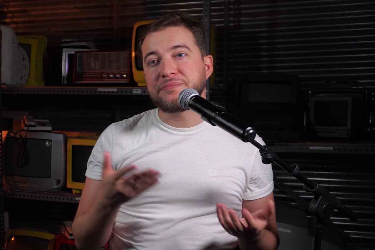 Presentador de podcast hablando ante un micrófono en un set decorado con televisores antiguos